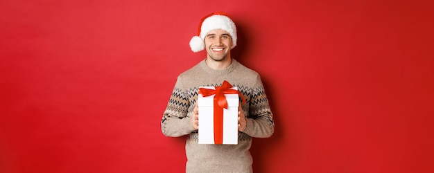 Imagen de hombre guapo sonriente con sombrero de santa y suéter de invierno sosteniendo un regalo dando navidad gif ...