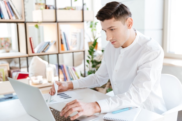 Imagen de hombre guapo vestido con camisa blanca con ordenador portátil. Trabajo colaborativo. Mirando la computadora.