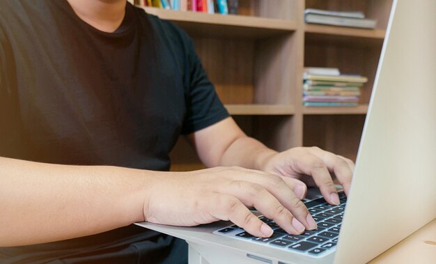 imagen de un hombre joven que trabaja en su computadora portátil en la biblioteca, vista trasera de manos de hombre de negocios ocupado utilizando equipo portátil en el escritorio de oficina, estudiante masculino joven escribiendo en equipo sentado en la mesa de madera