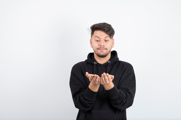 Imagen de hombre joven en sudadera con capucha negra de pie y posando