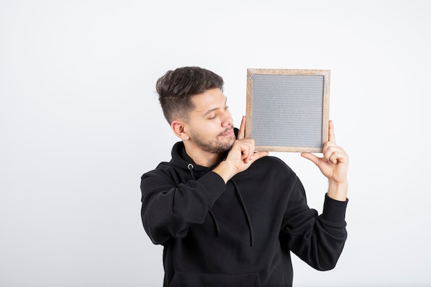 Foto imagen de hombre joven en sudadera con capucha negra que muestra el marco vacío