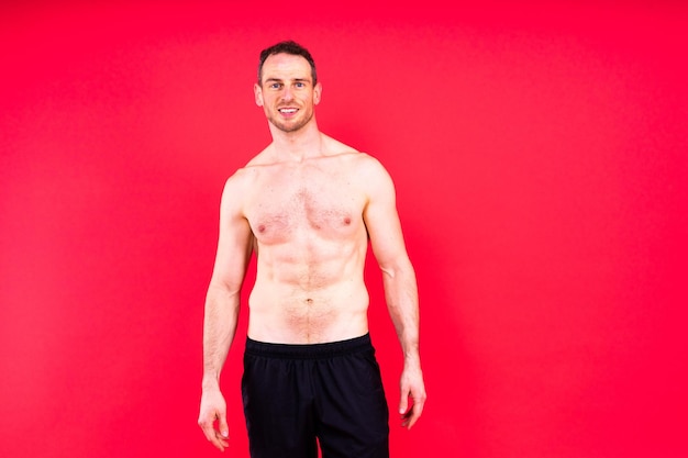 Foto imagen de un hombre musculoso posando en un estudio con fondo blanco oscuro y rojo