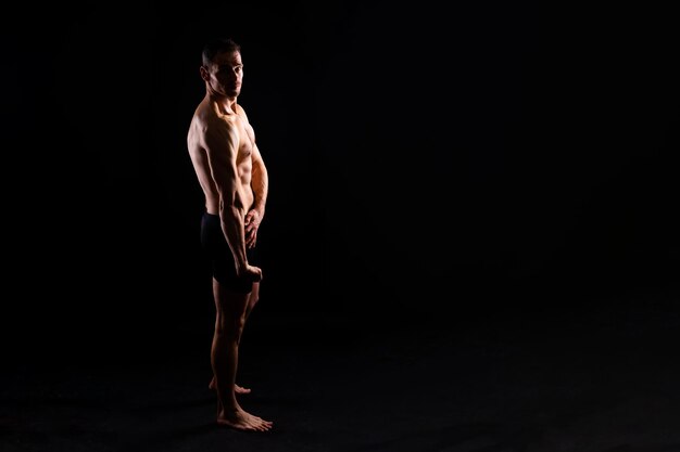 Imagen de un hombre musculoso posando en un estudio con fondo blanco oscuro y rojo