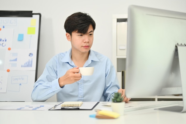 Imagen de un hombre de negocios asiático tomando café y trabajando en un proyecto de marketing en una oficina moderna