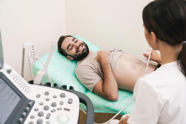 Imagen de hombre sonriente obteniendo ecografía abdominal por doctora en uniforme médico en el hospital