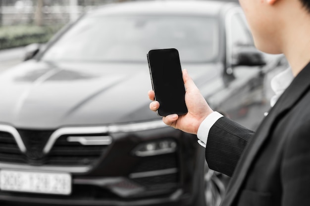 Imagen de un hombre sosteniendo un teléfono móvil frente a un automóvil