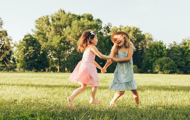 Imagen horizontal de dos niñas bailando sobre la hierba verde en el parque Niños disfrutando de los días de verano en el parque Dos hermanas divirtiéndose a la luz del sol al aire libre Concepto de infancia y amistad
