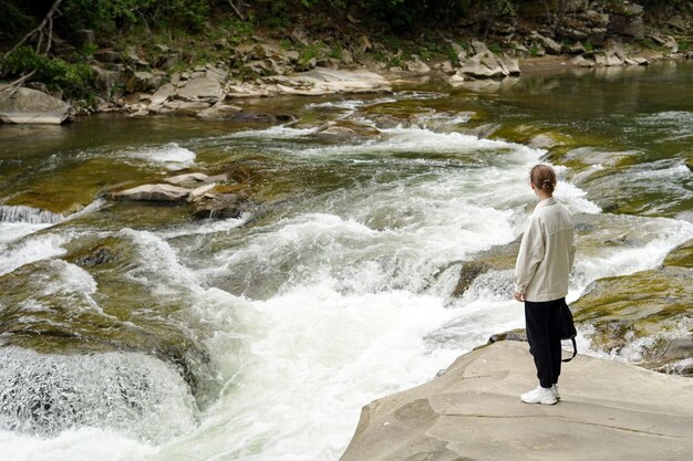 Imagen horizontal de una joven mujer elegantemente vestida cerca del río y los rápidos mirando la naturaleza Lugar para tu diseño