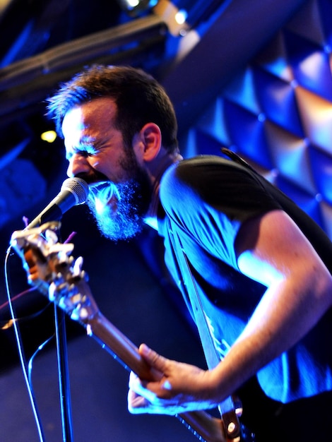 Imagen inclinada de un hombre cantando mientras toca la guitarra en un concierto.