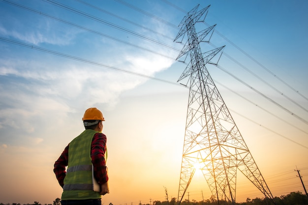 Imagen de un ingeniero eléctrico parado y observando en la estación de energía eléctrica para ver el trabajo de planificación produciendo electricidad en postes de electricidad de alto voltaje.