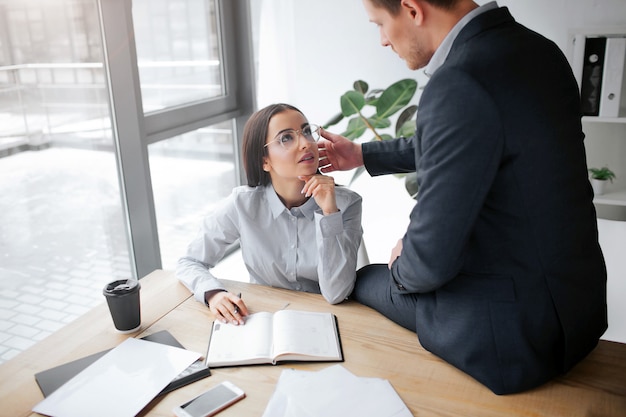 Imagen íntima de una encantadora joven sentada a la mesa y mirando a su jefe.