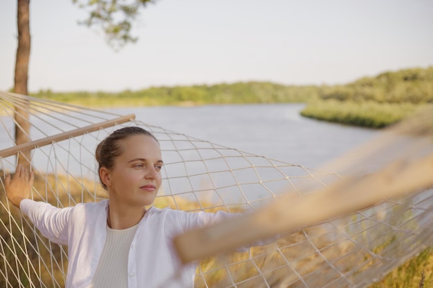 Imagen de una joven adulta caucásica con cabello oscuro y peinado de tapón con camisa blanca y pantalones amarillos mirando hacia otro lado disfrutando de la hermosa vista y la naturaleza