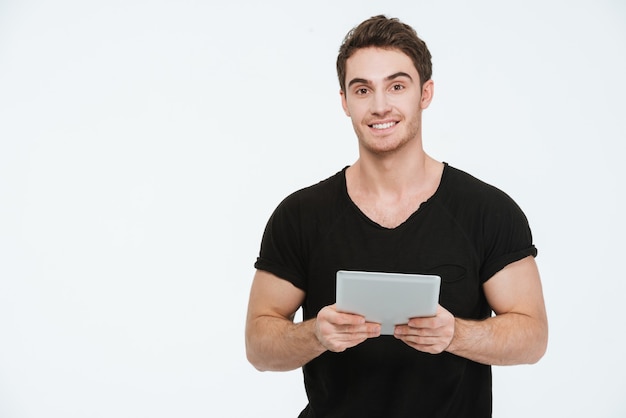 Imagen de joven alegre vestido con camiseta negra de pie sobre fondo blanco con tablet PC.