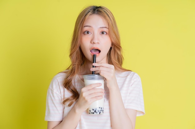 Imagen de una joven asiática bebiendo té con leche sobre fondo amarillo