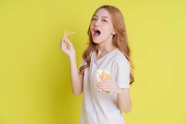 Imagen de una joven asiática comiendo papas fritas con fondo amarillo