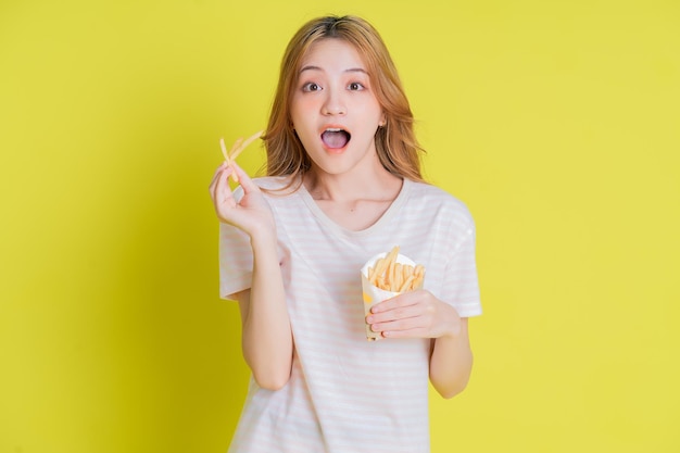 Imagen de una joven asiática comiendo papas fritas con fondo amarillo