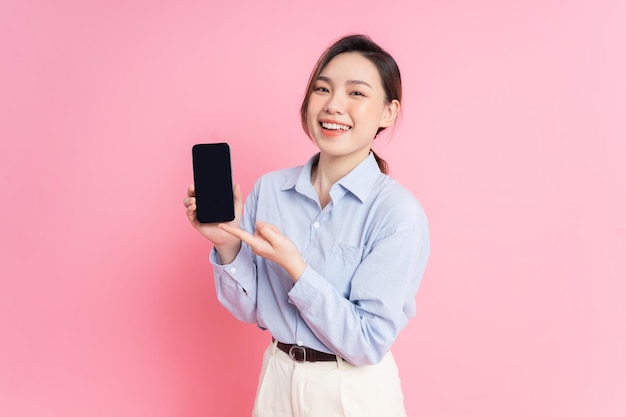 Imagen de una joven asiática sosteniendo un teléfono inteligente con fondo rosa