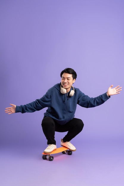 Imagen de un joven asiático jugando al skateboard en un fondo morado