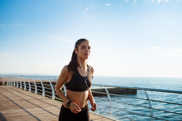 Imagen de una joven y atractiva chica fitness corriendo con la costa del mar al fondo