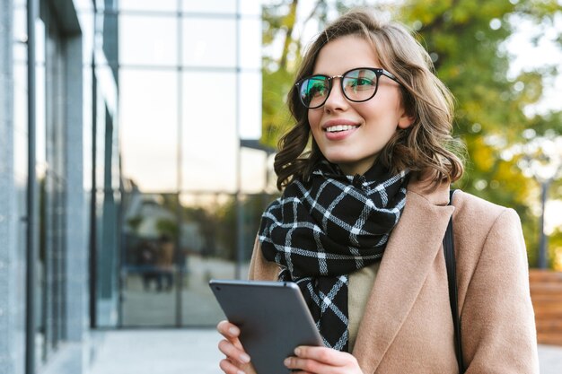 Imagen de una joven y bella mujer al aire libre caminando por la calle con tablet PC.