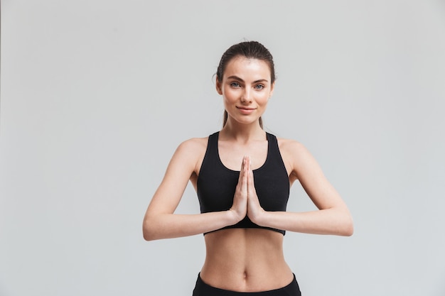 Imagen de una joven y bella mujer de fitness deporte hacer ejercicios aislados sobre pared gris meditar.