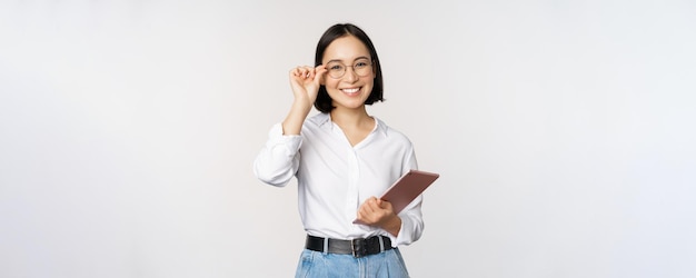 Imagen de una joven empresaria asiática empresaria con anteojos sosteniendo una tableta y luciendo profesional con anteojos de fondo blanco