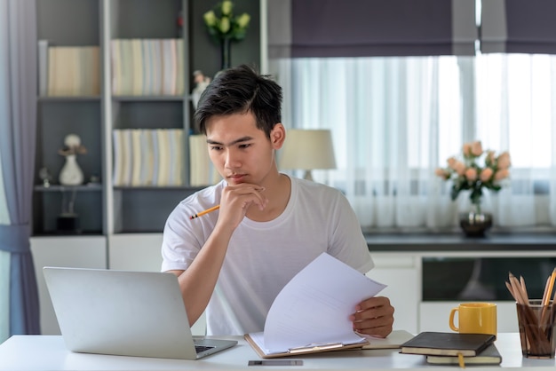 Imagen del joven empresario asiático analizando el trabajo usando una computadora portátil en casa.