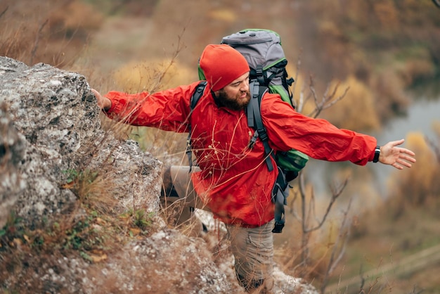 Imagen de un joven excursionista caminando por las montañas vestido con ropa roja explorando nuevos lugares Viajero barbudo trekking y montañismo durante su viaje Gente de viaje concepto de estilo de vida deportivo