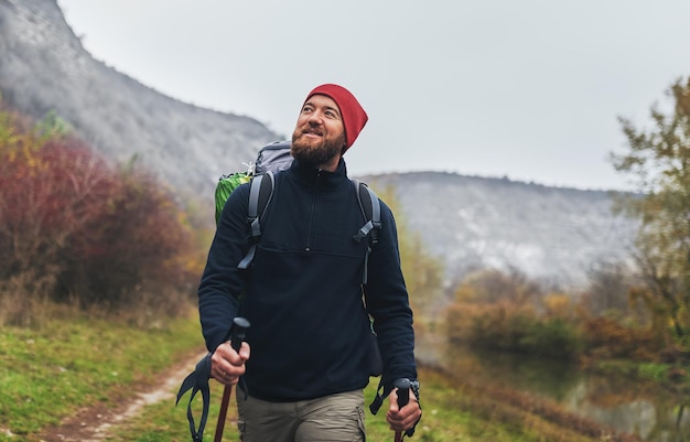 Imagen de un joven excursionista feliz caminando en las montañas con mochila de viaje Hombre viajero con barba trekking y montañismo durante las vacaciones Concepto de estilo de vida saludable para personas de viaje