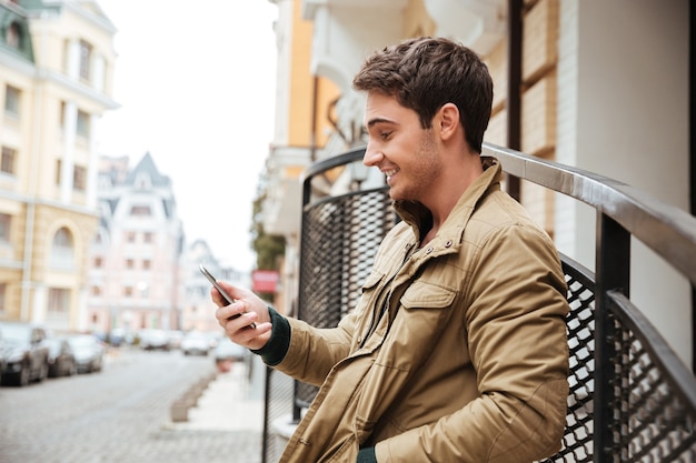 Imagen de joven feliz caminando por la calle y charlando por su teléfono al aire libre. Mira el teléfono.