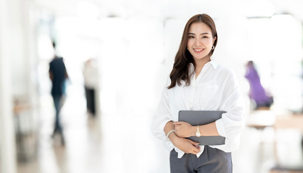 Imagen de una joven y hermosa mujer asiática trabajadora de una empresa con ropa informal sonriendo y sosteniendo una tableta digital de pie en el espacio de trabajo