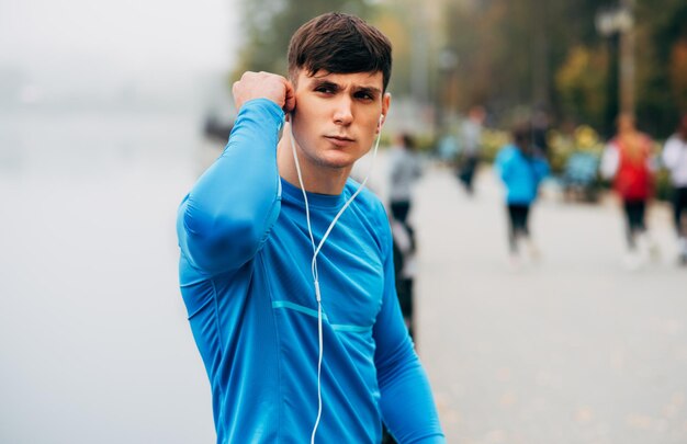 Imagen de un joven jogger musculoso que se estira al aire libre por la mañana en el fondo de la naturaleza de la niebla Fitness masculino haciendo ejercicio en el parque y escuchando la música en los auriculares Concepto de personas y deporte