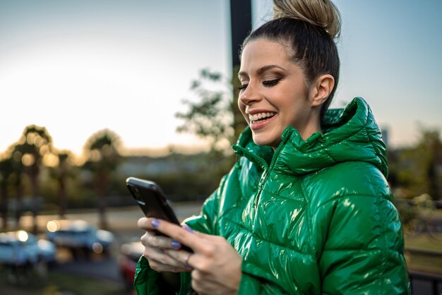 Imagen de una joven latina rubia emocionada feliz usando un celular en el fondo del parque