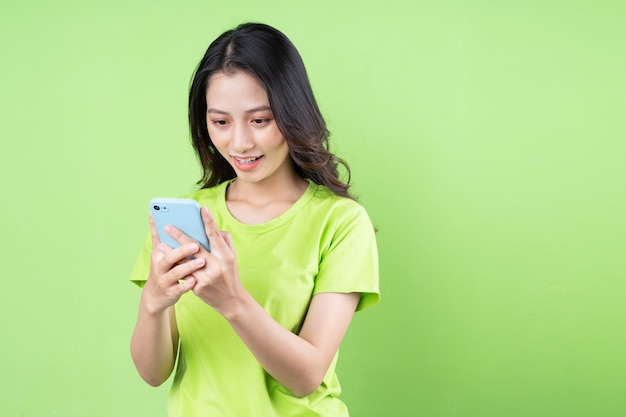 Imagen de joven mujer asiática sosteniendo smartphone sobre fondo verde