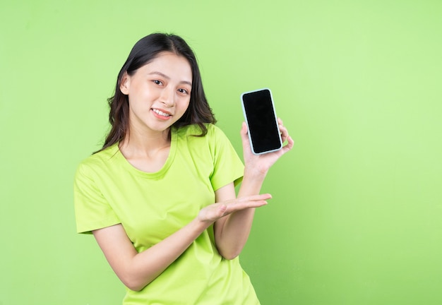 Imagen de joven mujer asiática sosteniendo smartphone sobre fondo verde