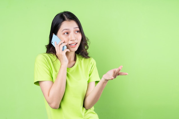 Imagen de joven mujer asiática sosteniendo smartphone sobre fondo verde