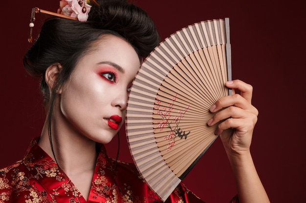 Imagen de la joven mujer geisha en kimono japonés tradicional sosteniendo un abanico de madera