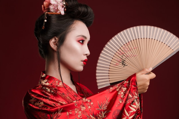 Imagen de la joven mujer geisha en kimono japonés tradicional sosteniendo un abanico de madera