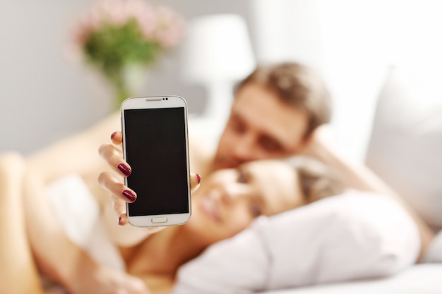 Imagen de la joven pareja abrazándose en la cama con smartphone