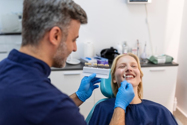 Imagen de una joven satisfecha sentada en un sillón dental en un centro médico mientras un médico profesional le arregla los dientes Una dentista eligiendo sombra de relleno para una mujer sonriente usando una muestra de escala dental