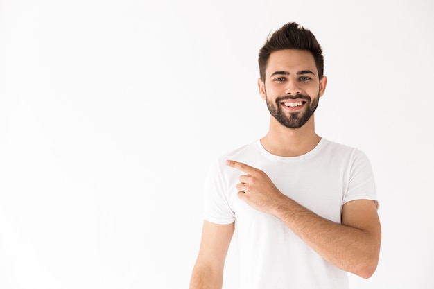 Imagen de un joven sonriente mirando y señalando con el dedo a un lado en el copyspace aislado sobre la pared blanca