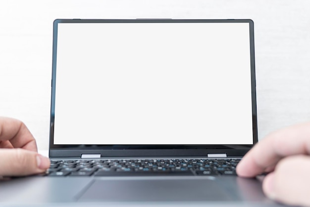Imagen de un joven trabajando frente a la computadora portátil mirando la pantalla con una pantalla blanca limpia y un espacio en blanco para texto y escribiendo información a mano en el teclado en el espacio de trabajo