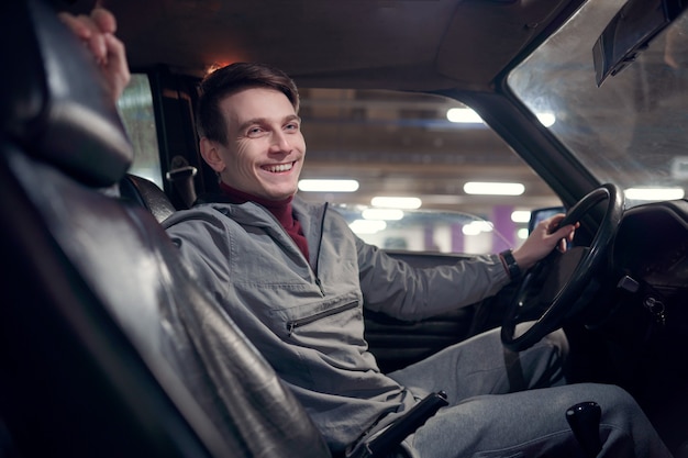 Imagen del lado del hombre feliz mirando a la cámara sentado en el coche