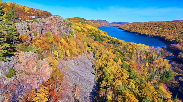 Imagen del lago gigante con acantilados rocosos, una pasarela de madera y un bosque en otoño