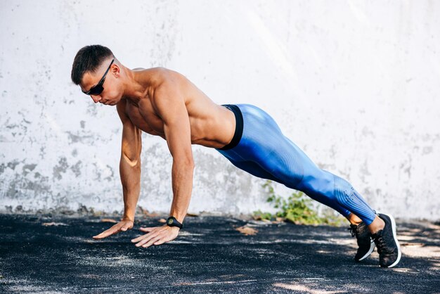 Imagen lateral de un hombre en forma fuerte haciendo ejercicio para el pecho al aire libre contra una pared de hormigón Copiar espacio para publicidad Deportista haciendo ejercicio de flexiones fuera