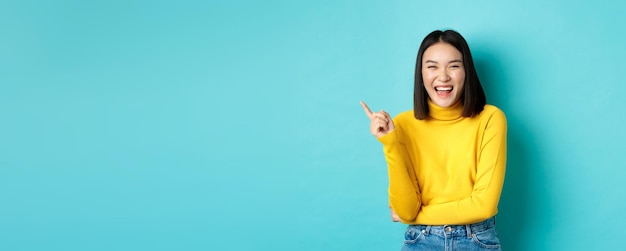 Imagen de una linda chica coreana despreocupada riéndose y luciendo feliz señalando con el dedo en la esquina superior izquierda