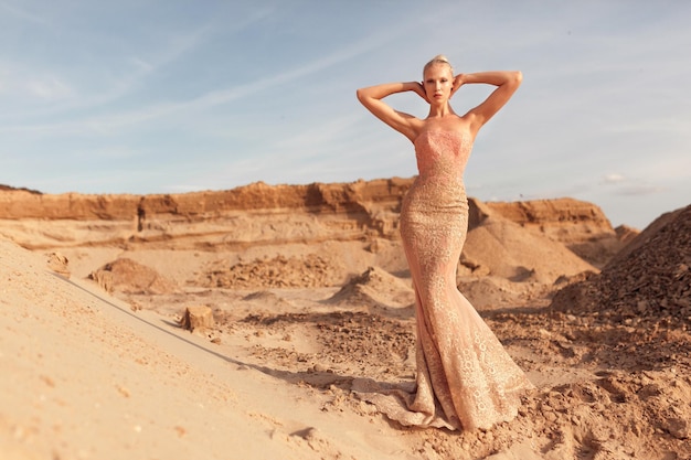 Imagen de longitud completa de una hermosa modelo femenina en un hermoso vestido delgado posando en el desierto al atardecer.