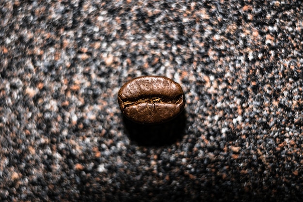 Imagen macro de un grano de café sobre una superficie con textura gris, pequeña profundidad de campo, enfoque selectivo