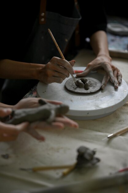 Imagen de la mano de un hombre usando una herramienta de escultura en arcilla cruda para crear formas