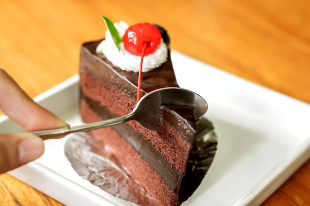 La imagen de la mano que sostiene una cucharadita está dividiendo un pastel de un pastel de chocolate en un plato de cerámica blanca a